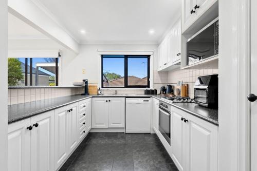 a white kitchen with white cabinets and a window at Central Geelong Escape Spa, Fire Pit, Sleeps 10 in Geelong