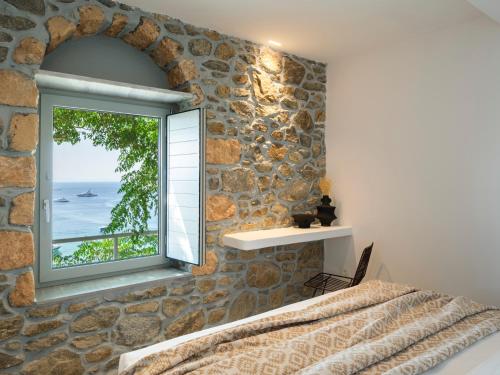 a bedroom with a stone wall and a window at Trinitas Mare Psarou Beach in Psarou
