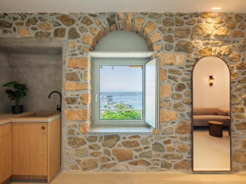 a bathroom with a stone wall with a window and a mirror at Trinitas Mare Psarou Beach in Psarou