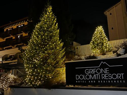 three christmas trees with lights in front of a sign at Grifone Dolomiti Resort in Arabba
