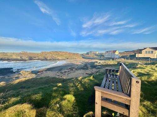 a wooden bench sitting on the side of a beach at GWYNFA-3 BED- GROUND FLOOR APT - SEA VIEWS - TREARDDUR BAY in Trearddur