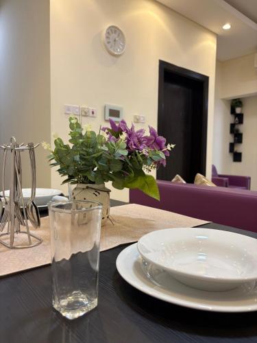 een tafel met een bord en een vaas met paarse bloemen bij Spacious Suite in Jazīrat as Sāyah