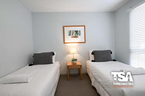 a room with two beds and a table with a lamp at Snowman 8 Penthouse in Thredbo