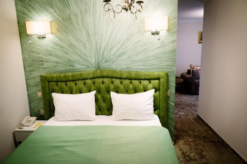 a bed with a green headboard and white pillows at Hotel-Restaurant La Belle Epoque in Petroşani