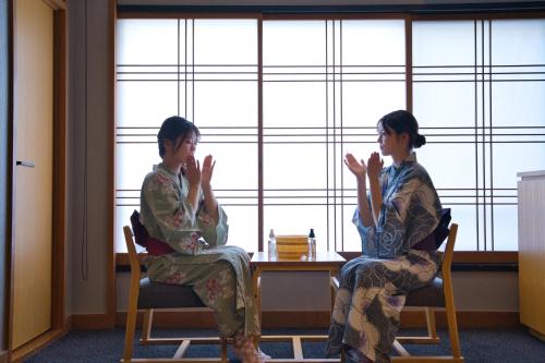 two women sitting in chairs in front of a window at Ito Kowakien in Ito