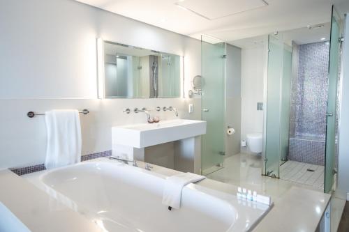 a bathroom with a tub and a sink and a shower at Blaauwberg Beach Hotel in Bloubergstrand