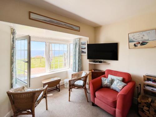 a living room with a red chair and a flat screen tv at Coastguard Cottage in Downderry