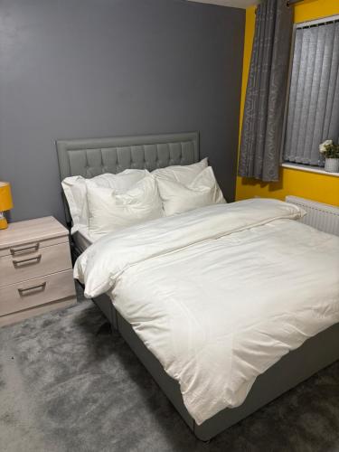 a bedroom with a bed with white sheets and a nightstand at Ellas Stays in Farnworth