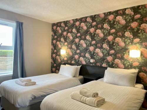 two beds in a room with a floral wall at The Weigh Inn Hotel & Lodges in Thurso