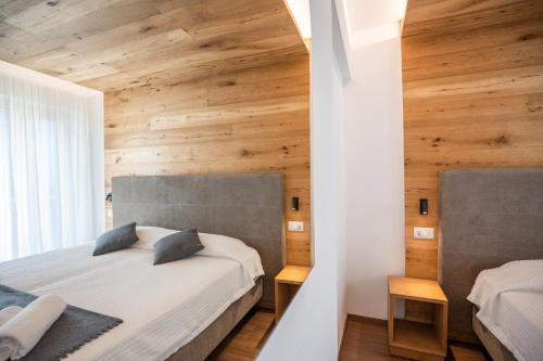 two beds in a bedroom with wooden walls at Albergo Silvana in Ledro