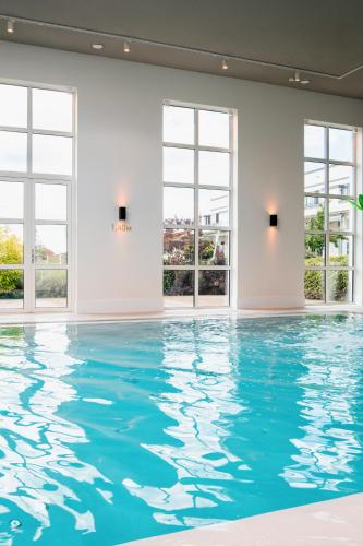 a swimming pool with blue water in a room with windows at Van der Valk Hotel Apeldoorn in Apeldoorn