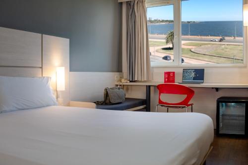 a hotel room with a bed and a desk and a window at ibis Montevideo Rambla in Montevideo