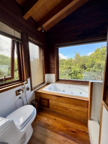 a bathroom with a tub and a toilet and two windows at Casa Arrayan in Puerto Varas