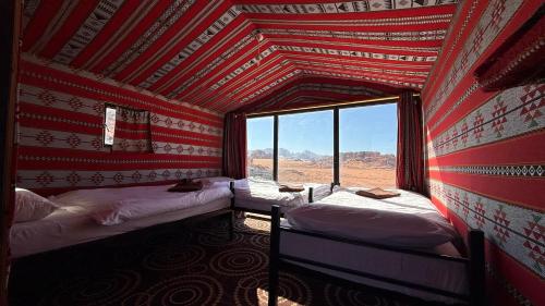 a room with two beds and a large window at Wadi Rum Trip Bedouin Camp in Wadi Rum