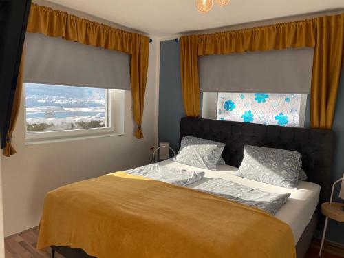 a bedroom with a bed with yellow sheets and two windows at Rosentalferien in Ludmannsdorf