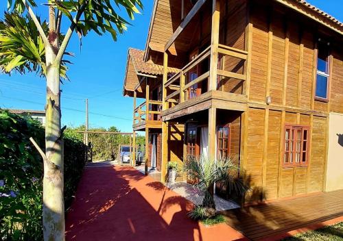 a wooden building with a palm tree in front of it at Hospedaria Chalés Rota Do Sol PDR - Aluguel de chalés confortáveis na Praia do Rosa SC in Praia do Rosa