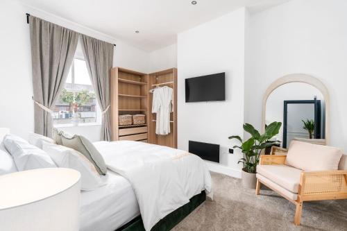 a white bedroom with a bed and a chair and a mirror at Luxury High-Ceiling Apartment Central Altrincham in Altrincham