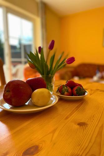 two plates of fruit on a wooden table with a vase of flowers at Backhuus 2 in Fehmarn