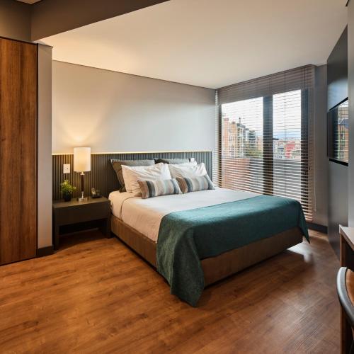 a bedroom with a large bed and a large window at Nico Apartasuites in Bogotá