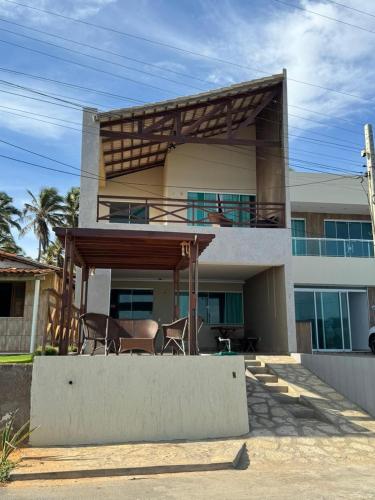 a house with a balcony with chairs in front of it at Casa da Maré Pé na areia Suítes climatizadas e deck vista mar in Icapuí