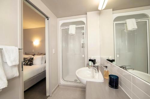 a bathroom with a sink and a shower and a bed at Cranford Oak Motel in Christchurch