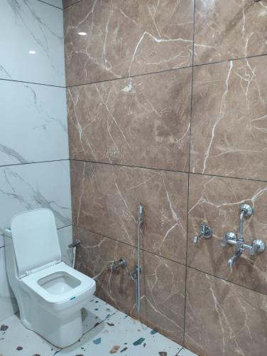Un baño con inodoro y pared de azulejos. en Hotel maya's, en Bāghpat