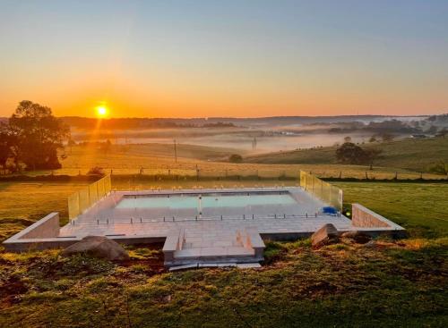 a swimming pool in a field with the sunrise at Milton Woodstock Homestead Luxury retreat with NEW 11M POOL just minutes from the beach in Milton