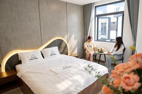 two women sitting in a hotel room with a bed at Vinh Home Apartment in Quang Tri
