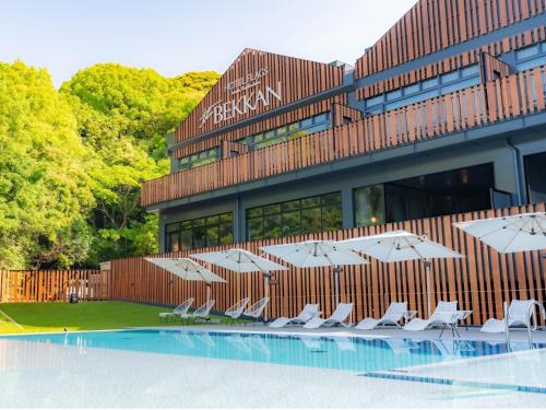 a building with chairs and umbrellas next to a pool at Hotel Flags Sasebo KujuKusima in Sasebo