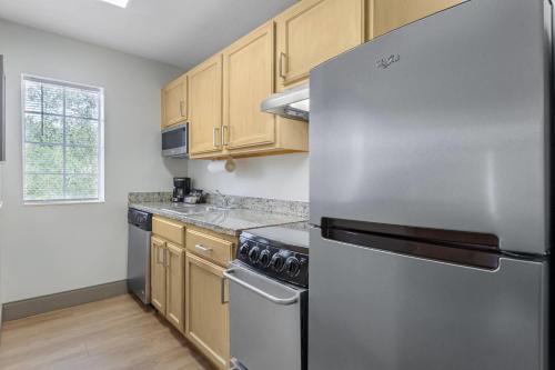 a kitchen with a stainless steel refrigerator and wooden cabinets at MainStay Suites Tampa Moffitt-USF in Tampa