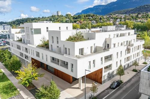 an image of a white building with mountains in the background at Zenitude Hôtel-Résidences Chambéry in Chambéry