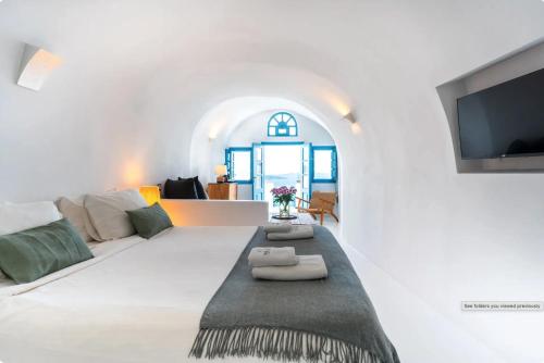 a white living room with a couch and a tv at Anemos Caldera Oia in Oia