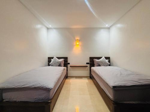 two beds in a room with a light on the wall at Inass appartement in Essaouira