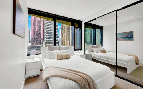 a white bedroom with two beds and large windows at Luxurious 2BR Apartment - Central CBD Location with Pool, Gym in Melbourne