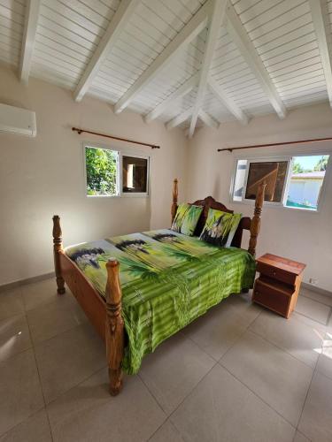a bedroom with a bed with a green comforter and two windows at Maison de vacances in Deshaies