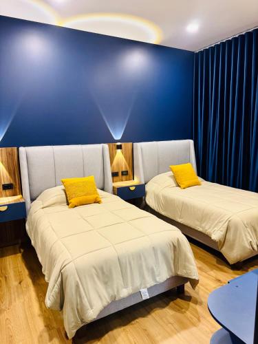two beds in a room with blue walls and yellow pillows at Departamento de lujo inteligente in Cochabamba