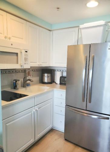 a kitchen with white cabinets and a stainless steel refrigerator at Sunkissed-Modern Oceanfront Condo Daytona Beach in Daytona Beach