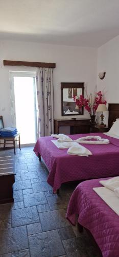 a bedroom with two beds with purple sheets and a mirror at Rita's Place Hotel in Ios Chora