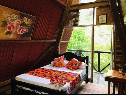 a bedroom with a bed with colorful pillows and a window at Hotel Eco Point in Minca