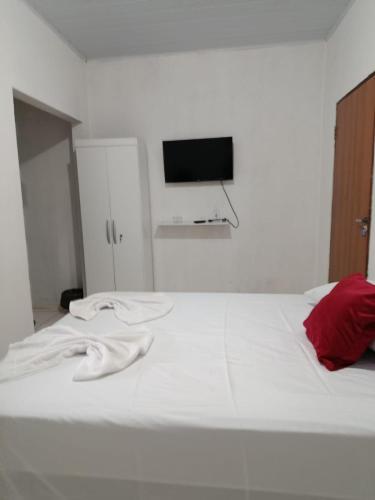 a white bed with a red pillow and a flat screen tv at hospedagem dos viajantes in Lençóis