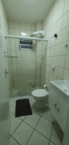 a white tiled bathroom with a toilet and a sink at Murilo House - Apart-hotel completo e privativo in São José