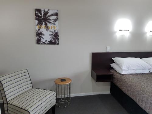 a bedroom with a bed and a chair and a table at Aspree Motor Inn in Palmerston North