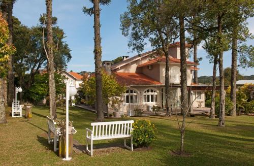 a white bench in front of a house with trees at Doce Canela - Pousada de Charme in Canela