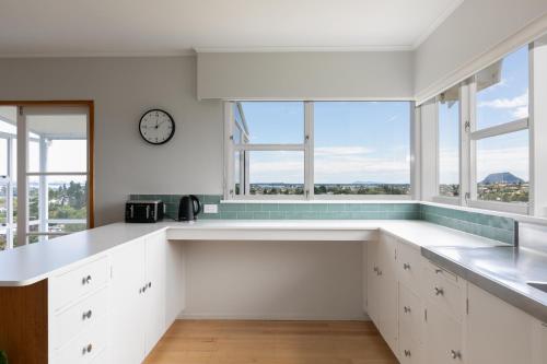 a white kitchen with windows and a clock on the wall at The Hilltop Hideaway in Tauranga