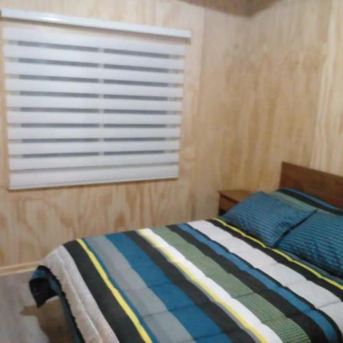a bedroom with a bed and a window with blinds at Cabañas Uenke in Puerto Puyuhuapi