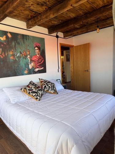 a bedroom with a white bed with a painting on the wall at La Escondida Cabañas in Mineral del Monte
