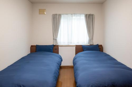 two blue beds in a room with a window at Furano Ski Frante 2 in Furano