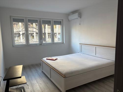 a white bedroom with a bed and two windows at Capital Gate Guest House in Skopje
