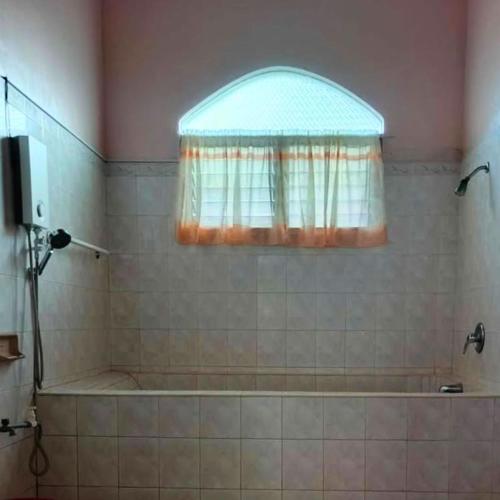 a bathroom with a tub and a window and a shower at Alaba Vacation House w Pool and Beach Access in Mambajao