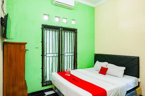 a green room with a bed with a red blanket at RedDoorz near RSUD Kebumen 2 in Wanasari